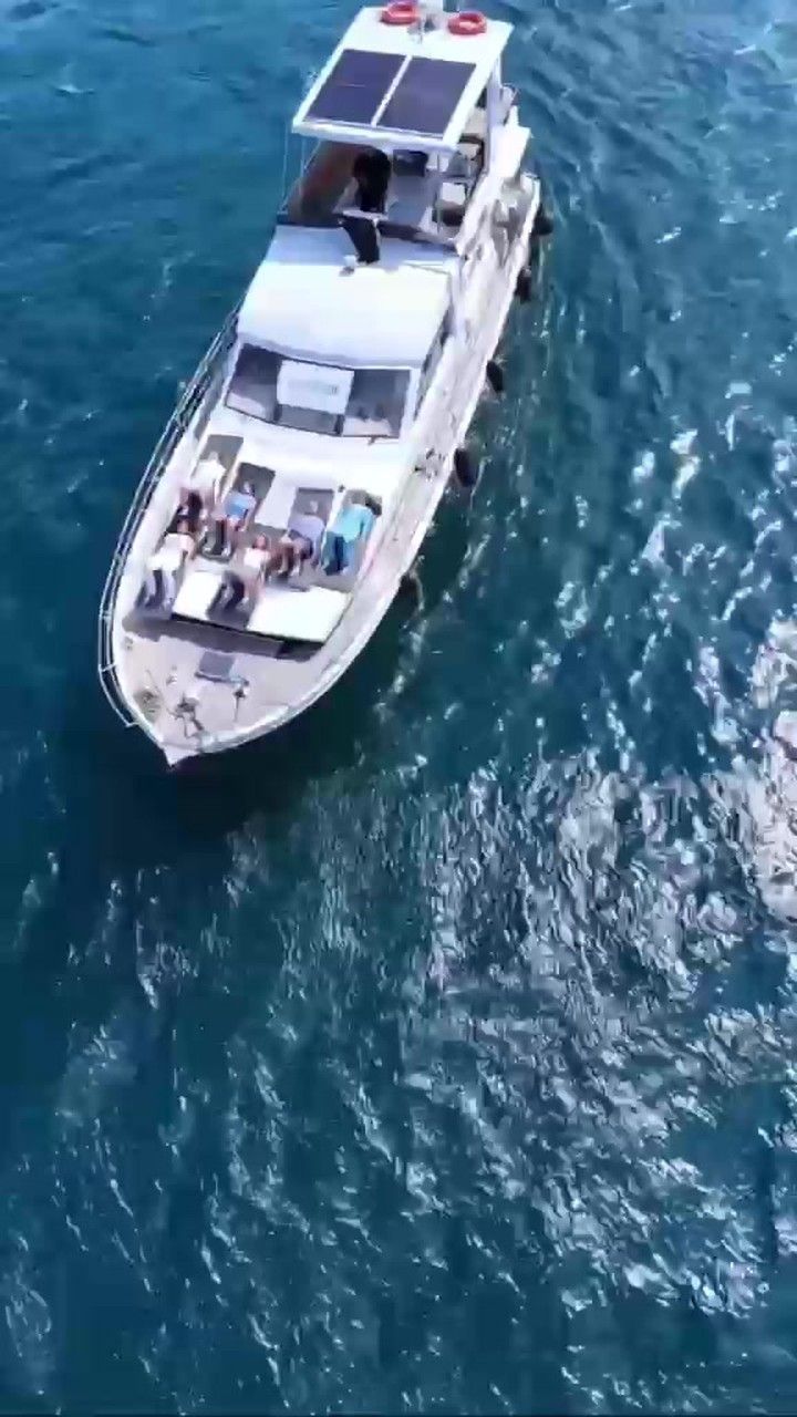 Mavi denizde ilerleyen beyaz bir teknenin yukarıdan çekilmiş görüntüsü.